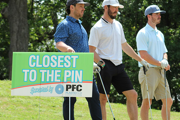 Golfers stand by a sponsor sign for PFC at the Dallas golf event.