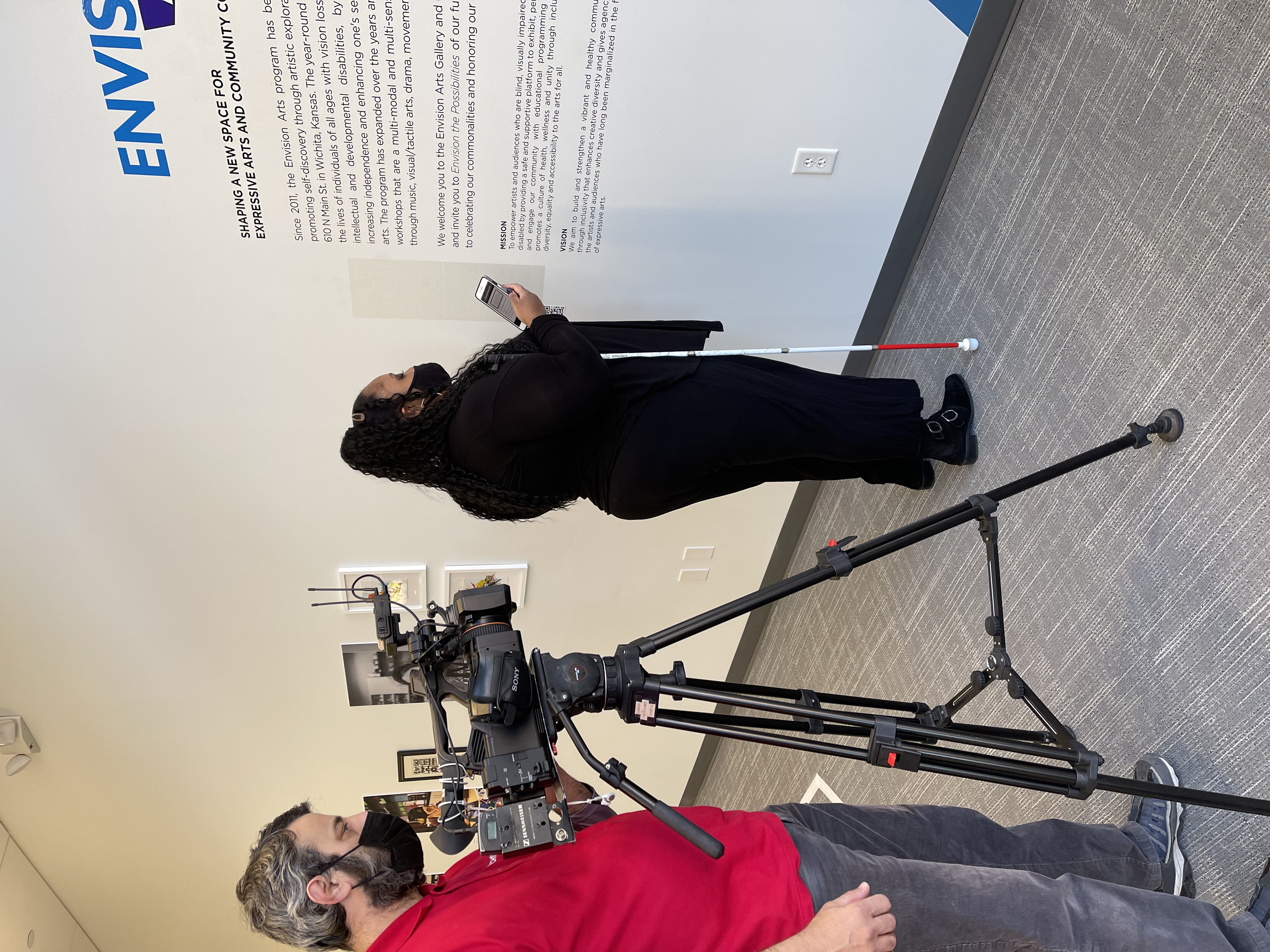 Envision Arts artist Ciara scans QR code in the art gallery while a TV crew captures it on video