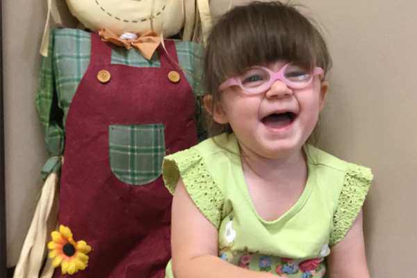 Dallas wearing a light green top laughs at the camera sitting by a stuffed scarecrow.