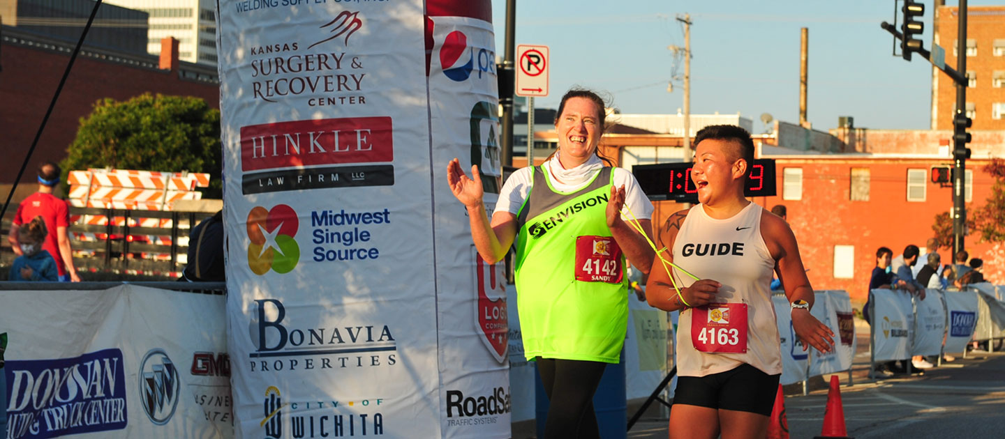 Envision employee Sandy crosses the finish line with her guide in the Prairie Fire marathon.