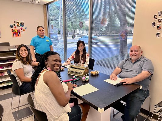 A group of people are sitting at a black table learning how to read braille. 