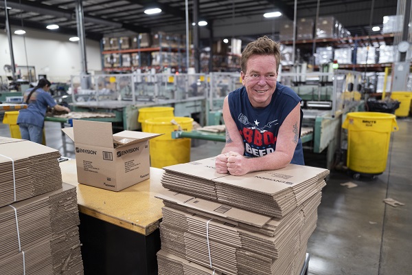 Envision manufacturing employee Kelly Leonard leaning on a pile of boxes and smiling on the manufacturing floor
