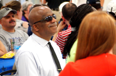 A smiling man wearing black sunglasses sits at one of the tables at Evening with Envision.