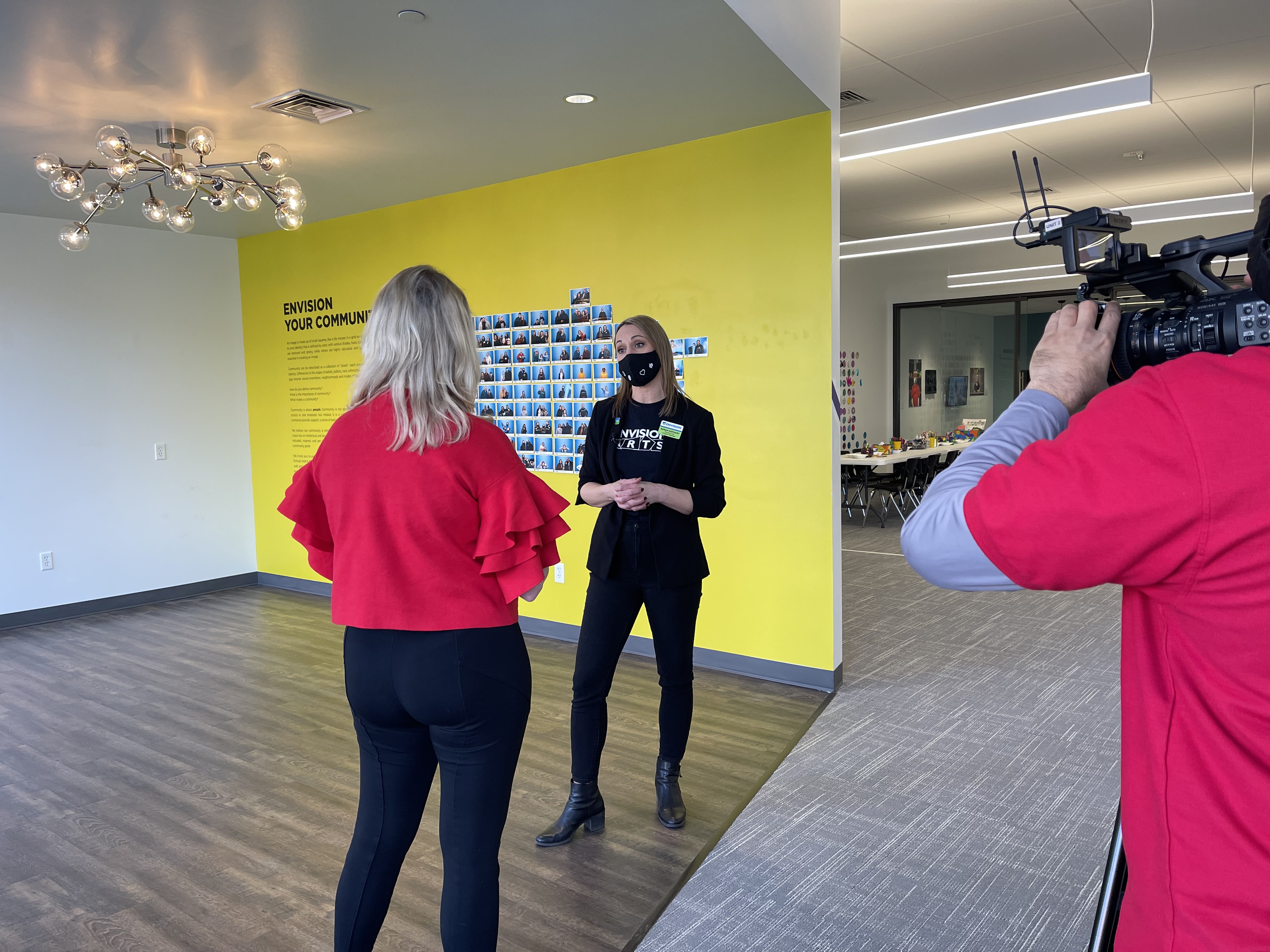 Sarah Kephart standing in front of a yellow wall being interviewed by a local TV station