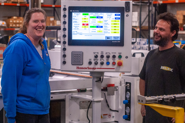 Sandra stands with coworker Russel by a bagging machine at Envision Industries.