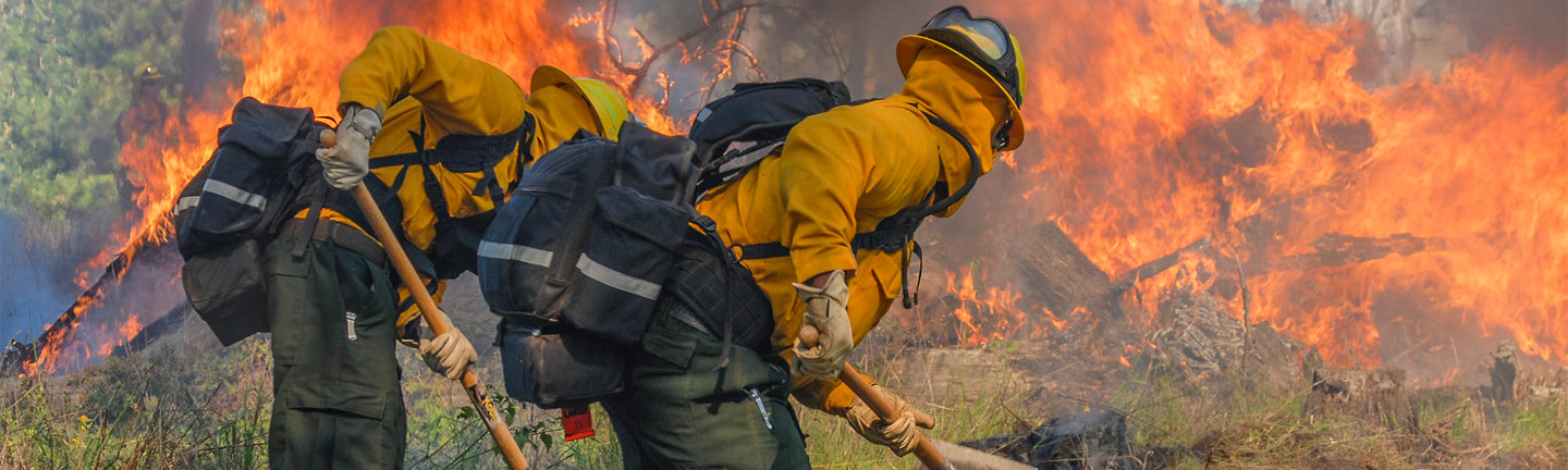 Two firefighters in their safety suits fighting a fire outside