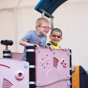 Two young boys with glasses playing on a slide.