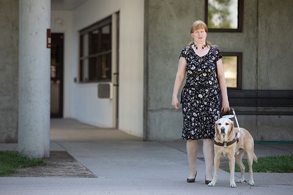 Woman who is blind walks outside of the Envision building with her guide dog.