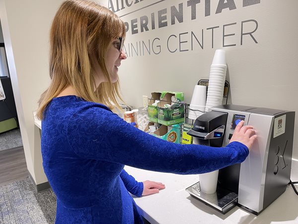 A woman who is visually impaired in a blue shirt using a Keurig machine. 