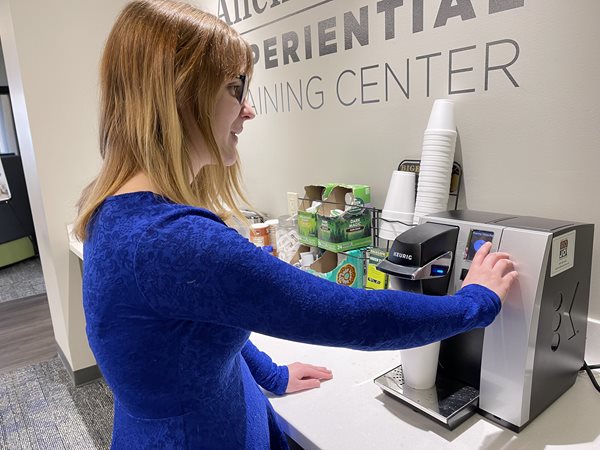 How Someone Who is Blind or Visually Impaired Gets Ready in the Morning A woman who is visually impaired in a blue shirt using a Keurig machine.