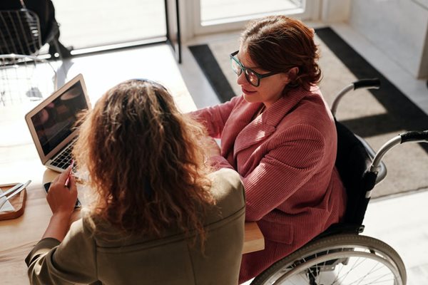 Two women working together at a desk, one woman is in a wheelchair. 