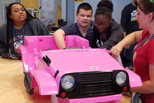 Students at Level Up work together building an electrical child size pink jeep at the Go Baby Go project for WSU.