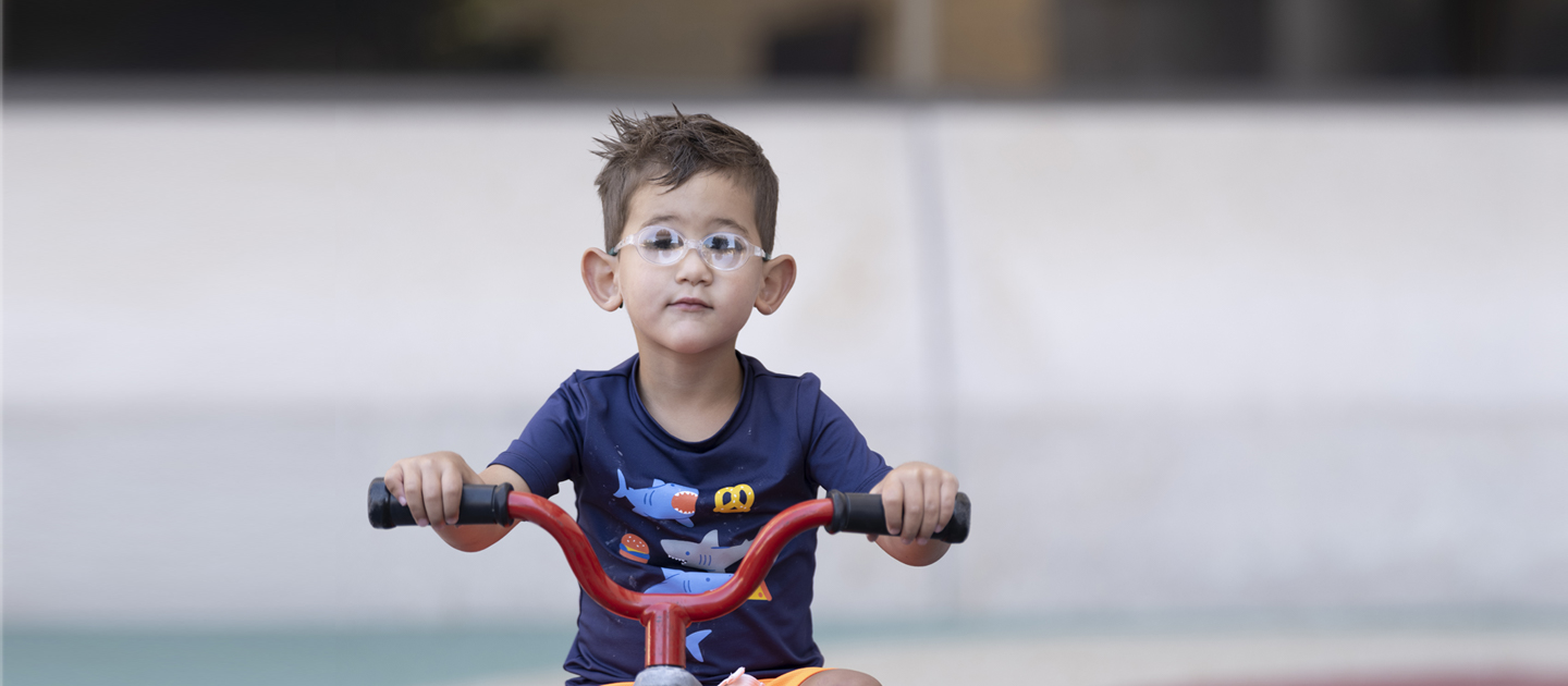 Little boy who is visually impaired rides a trike on the playground at ECDC.