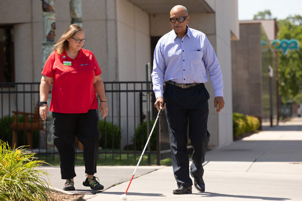 Man who is visually impaired receives training with his white cane from an O&M specialist.