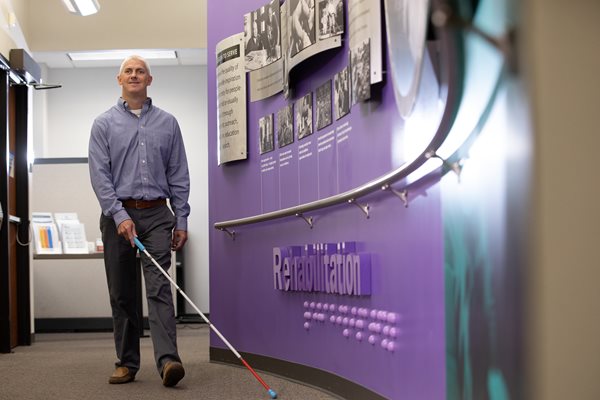 Man who is visually impaired smiling while walking the halls of Envision with his white cane