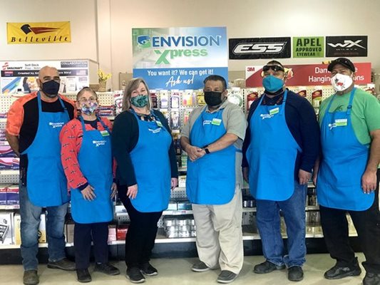 A group of people from the Lemoore Base Supply Store in their blue aprons smiling for the camera. 