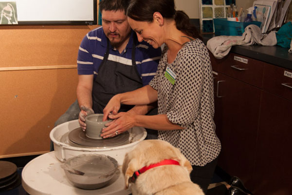 Sarah, Envision Art Teacher and therapist, assists a student at the pottery wheel.