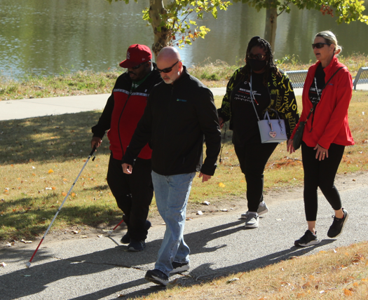 Four people, one has a white cane, one is Ray Oddis, walk happily down a sidewalk