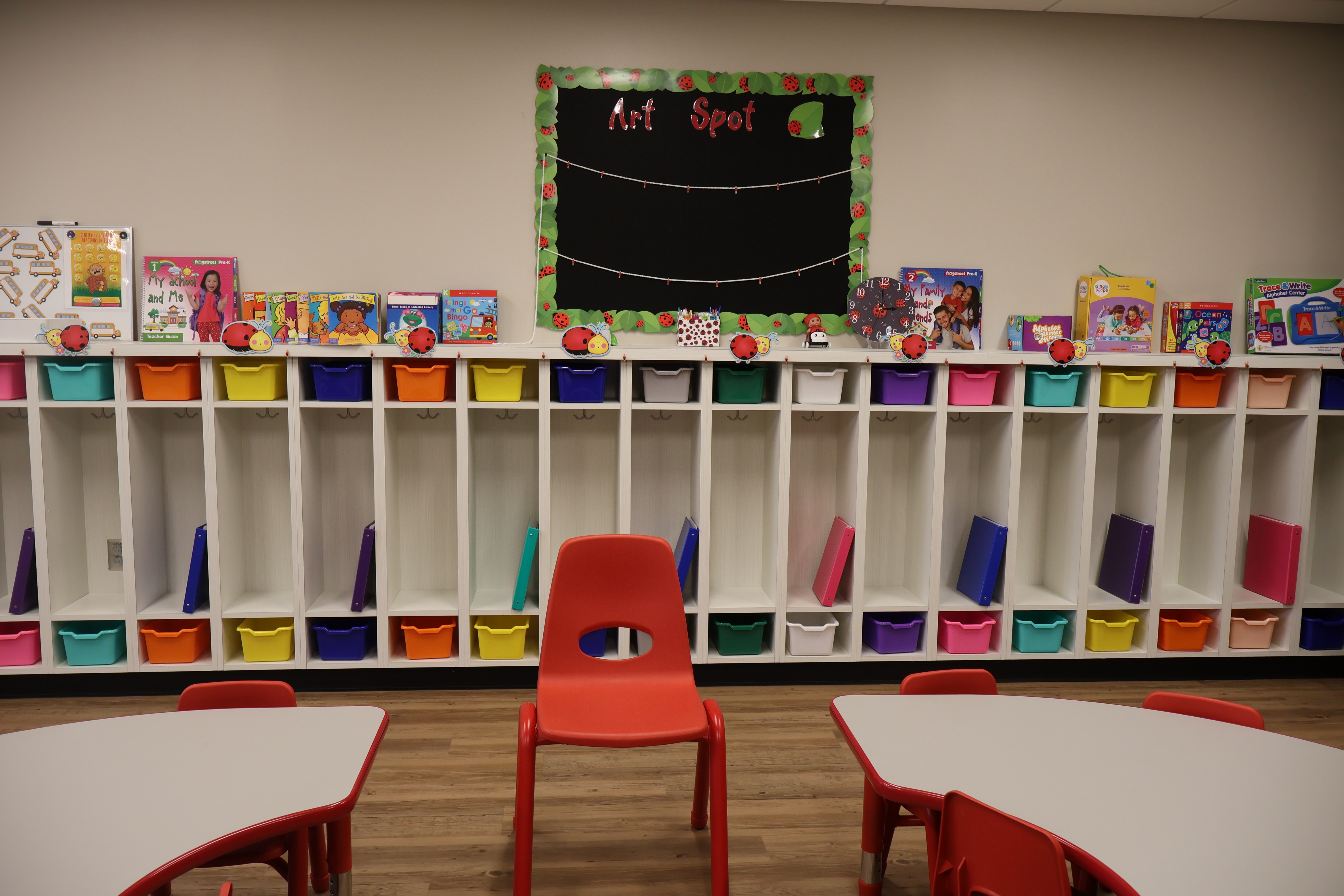 A bright, welcoming classroom art area with colorful cubbies filled with folders, children’s books on top, and kid-sized tables and chairs creating an inclusive, inviting space for all learners.