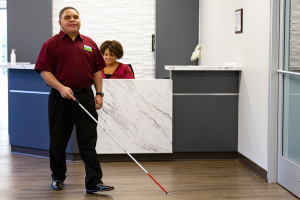 Man who is blind navigates with his white cane through the front lobby at Envision Dallas.