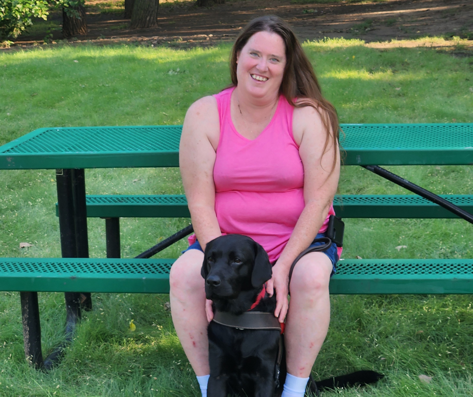 Sandy Wilkinson sitting on a park bench with her guide dog Darwin
