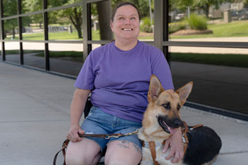 Lady sitting down with her guide dog outside and smiling