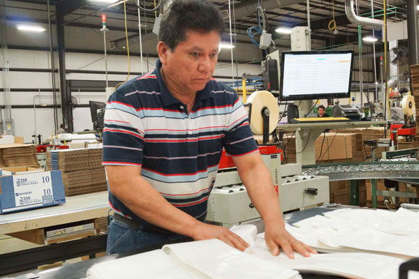Finding Hope Jose working at Envision Industries folding plastic bags to be boxed for shipping.