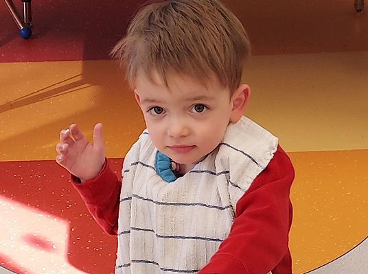 A young boy with glasses on posing for the camera while eating a green frosted cupcake. 