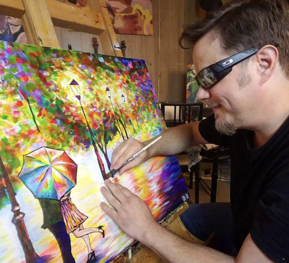 John Bramblitt painting a colorful image of two people hiding behind an umbrella
