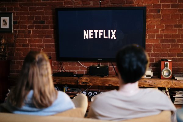 Two people sitting on the coach about to watch Netflix on TV