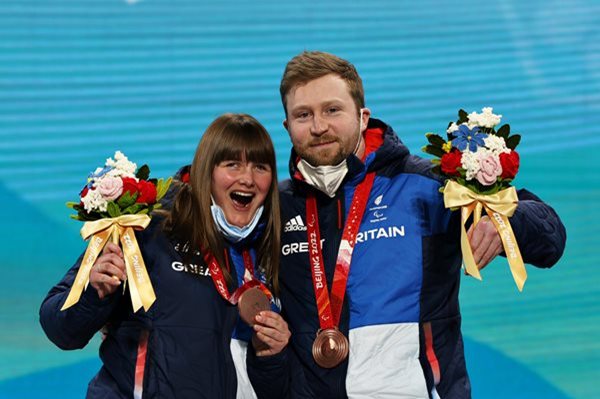 A women and a man stand together holding up bronze medals that they won.