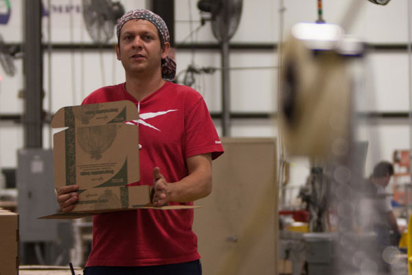 Paco wearing a bandana folds a box at his job at Envision Industries.