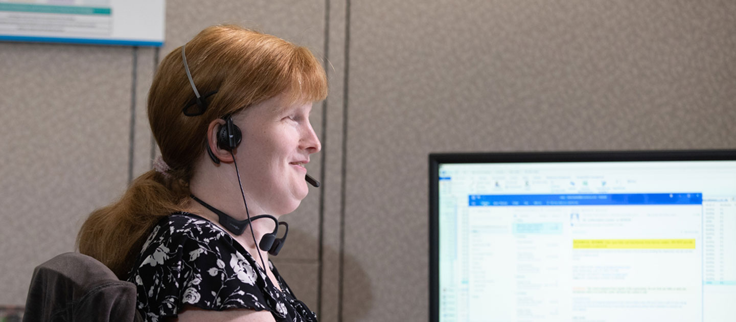 Woman with red hair who is blind chats with a customer at her customer service job.