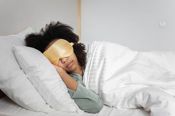 Woman sleeping on a bed with white blanket with a gold eye mask over her face